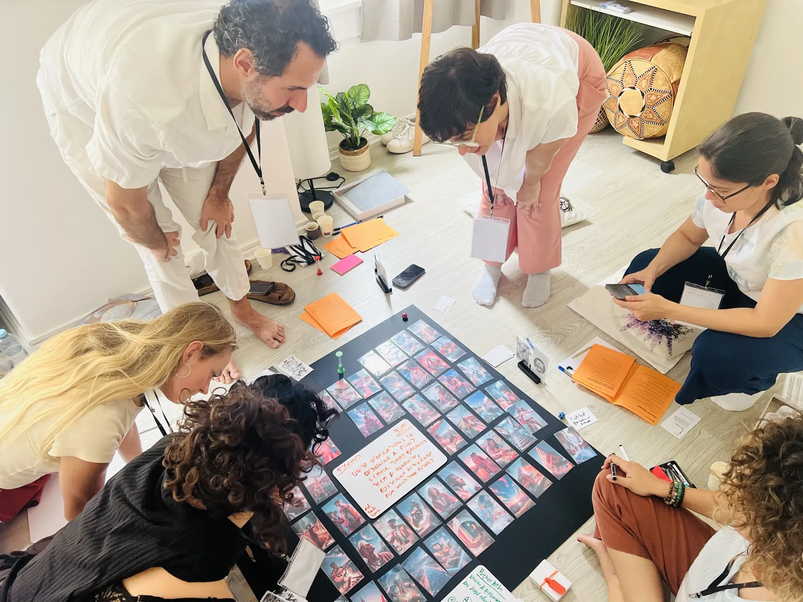 Workshop no estúdio: participantes à volta de um tabuleiro de cartas no chão, a discutir ideias para o futuro